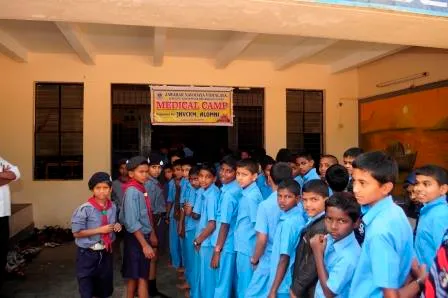 ವೈದ್ಯಕೀಯ ಶಿಬಿರದ ಬ್ಯಾನರ್ ಕೆಳಗೆ ಶಾಲಾ ಕಟ್ಟಡದ ಹೊರಗೆ ಸಾಲಾಗಿ ನಿಂತಿರುವ ವಿದ್ಯಾರ್ಥಿಗಳು.