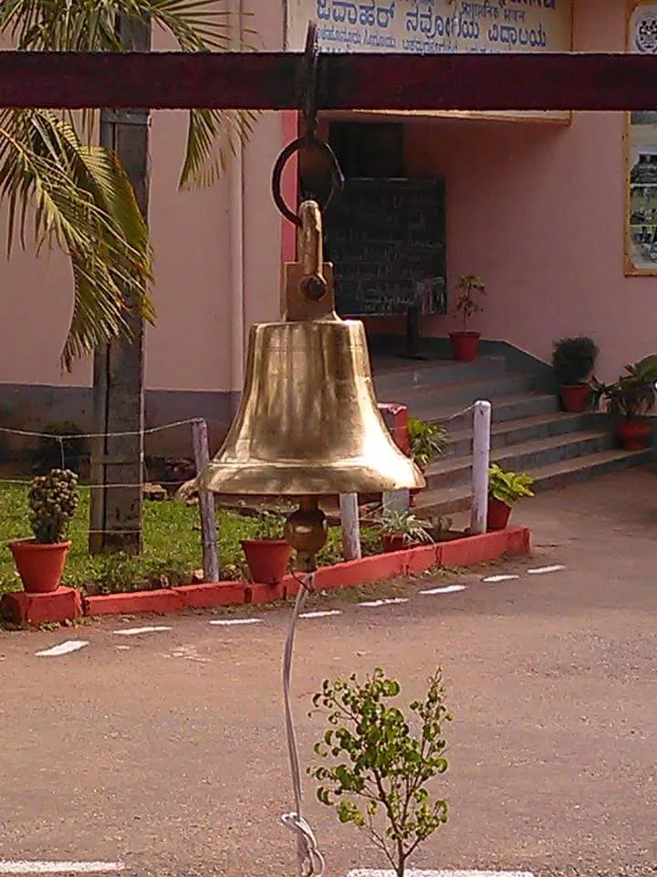 ಶಾಲಾ ಕಟ್ಟಡದ ಮುಂಭಾಗದಲ್ಲಿ ಕಂಬಿಯಿಂದ ತೂಗುಹಾಕಿರುವ ಕಂಚಿನ ಗಂಟೆ.
