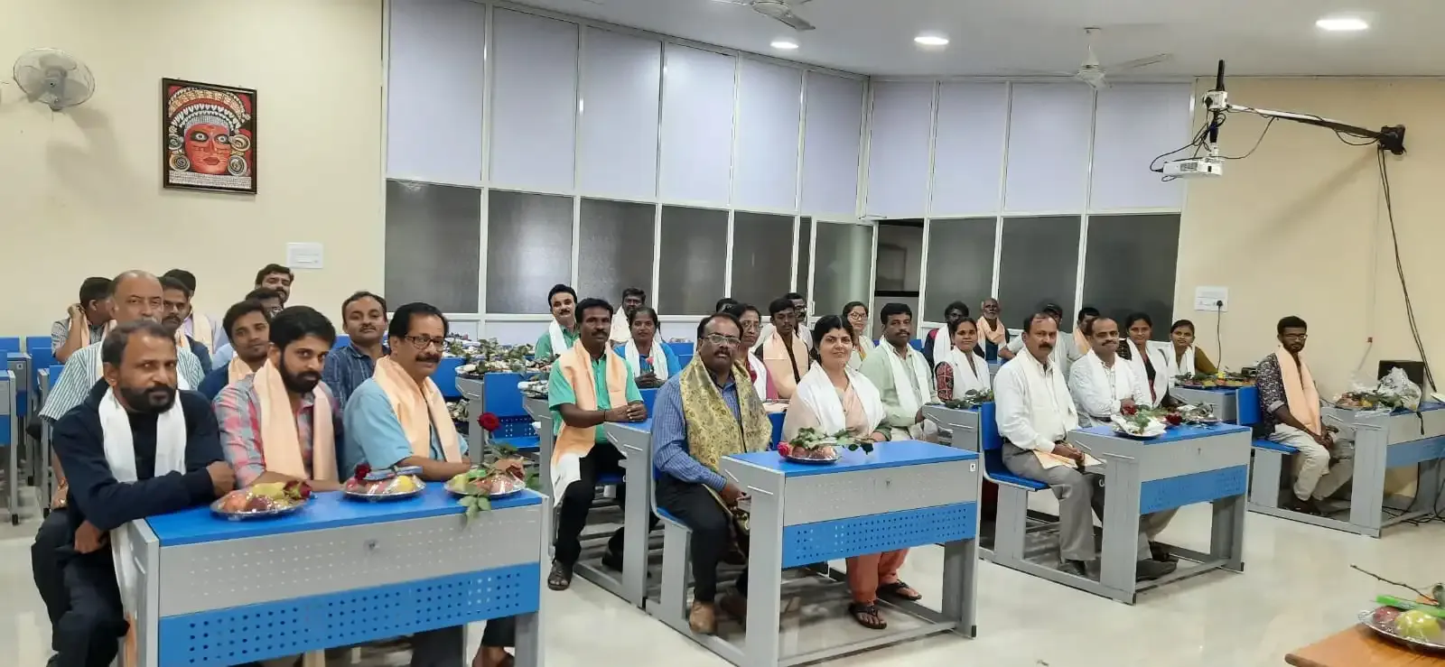ಸನ್ಮಾನ ಸಮಾರಂಭದಲ್ಲಿ ಶಾಲು ಹೊದಿಸಿದ ಶಿಕ್ಷಕರು ಮತ್ತು ಅತಿಥಿಗಳು ಮೇಜುಗಳಲ್ಲಿ ಕುಳಿತಿದ್ದಾರೆ.